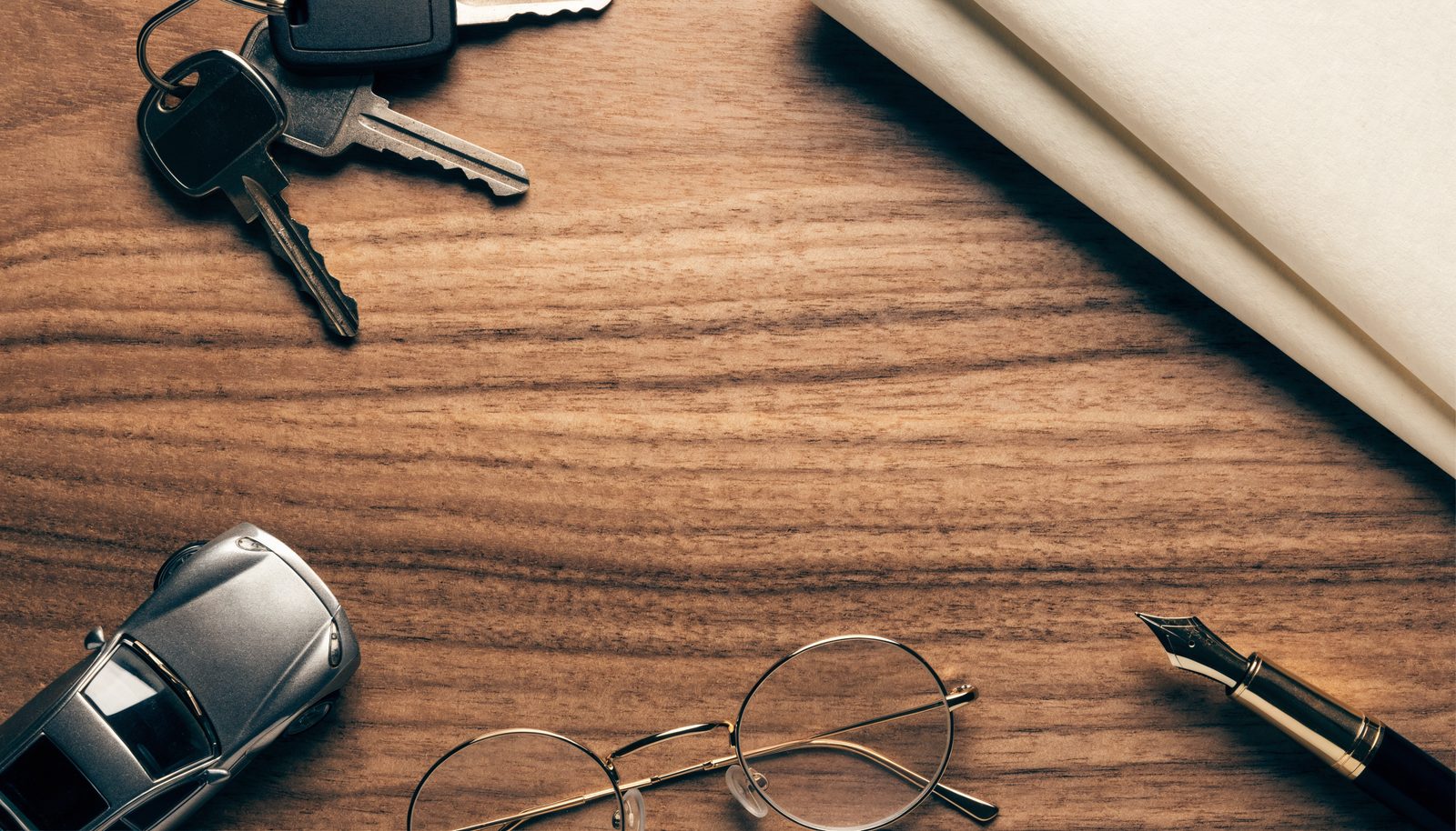 Car keys, an auto insurance policy, and a pen arranged on a desk